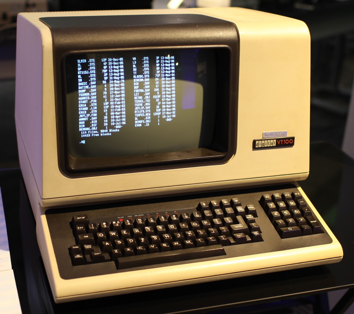 Un terminal informatique DEC VT100 : un écran cathodique beige posé sur son clavier, qui affiche une liste de fichiers.